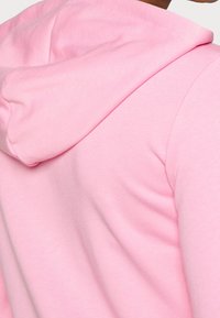 Sudadera ligera de color rosa con capucha ajustable, hecha de una suave mezcla de algodón y con una textura lisa, resaltando la forma redondeada de los hombros.