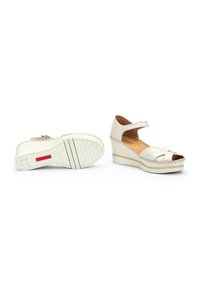 Sandales compensées blanches avec un bout ouvert, des brides croisées et une lanière de cheville. Présente des détails de bord tressés et une semelle texturée avec un motif en zigzag.