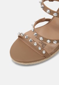 Sandale nue à brides avec des clous métalliques argentés, un dessus en cuir lisse et une semelle de style espadrille texturée.