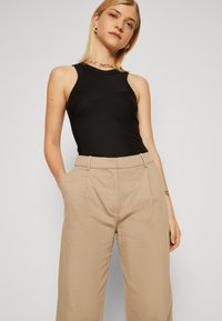 Top negru fără mâneci cu textură ribbed, asortat cu pantaloni bej cu croială largă, dintr-un material neted, având detalii de pliu pe față.