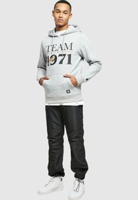 Hanorac gri cu imprimeu "TEAM 1971", buzunar tip kangaroo și glugă cu șnur; asortat cu pantaloni negri și adidași albi.
