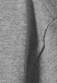 Gray fabric texture featuring a soft, knitted appearance with a subtle heather pattern and visible stitching along the edges.