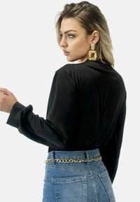 Svart satinblus med långa ärmar, lös passform och rundad halsringning. Kombinerad med blå denimjeans som har ett bälte av guldkedja.