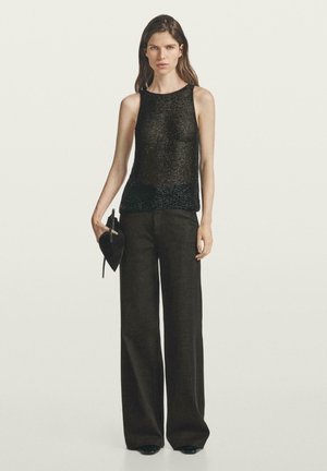 Un pull noir sans manches avec un tricot texturé et des accents scintillants à l'ourlet, associé à un pantalon large taille haute de couleur sombre.