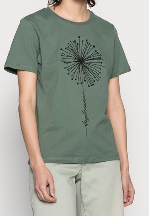 Person iført en grøn kortærmet t-shirt med en sort mælkebøttegrafik og ordet "daydreamer" foran.