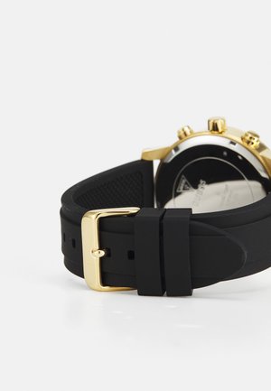 Mustmust mustrik, millel on kuldne metallist pandla, tekstuuriga disain ja reguleeritavad augud, kinnitatud ümmarguse kellakupli külge.