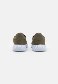 Baskets vert olive avec tige en tissu texturé, talon arrondi et semelle blanche texturée, présentant un design minimaliste et sans marque visible.