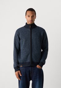 Pulover închis la culoare cu fermoar, cu model herringbone, manșete cu nervuri, guler înalt și un sistem de prindere din lemn. Purtați peste blugi închiși.