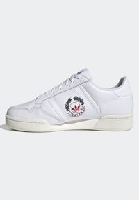 Sneaker bianco in pelle con superficie testurizzata, caratterizzato da tre strisce laterali, logo ricamato e suola in gomma bianca. Accenti rossi sulla linguetta.