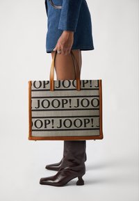 Sac fourre-tout avec une forme structurée, fabriqué en toile avec un motif répétitif "JOOP!" en noir, agrémenté de poignées et de finitions en cuir marron.