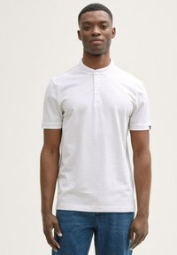 Witte polo met korte mouwen en een kraag met knopen. Gemaakt van een textuurstof, met een subtiel patroon en een zwart logo op de mouw.