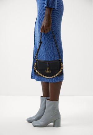 Bolso de mano de cuero negro con detalle de cadena dorada, forma rectangular, textura suave. Combinado con un vestido a rayas azul y botas grises de tacón.