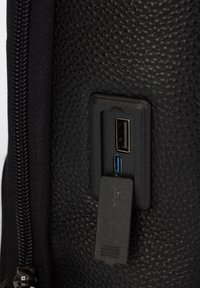 Musta teksturoitu pinta, jossa on USB-portteja, yksi tavallinen ja yksi sininen, kiinnitetty suorakaiteen muotoiseen mustaan muovipaneeliin. Vetoketjureuna näkyvissä.