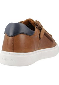 Zapatilla de cuero marrón con un acento de cuero azul en el talón, suela de goma blanca y detalle de cremallera lateral. Superficie texturizada con costuras sutiles.