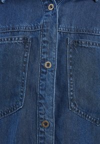 Denim srajca v temno modri barvi, ki ima dve sprednji žepi, zapiranje na gumbi in kontrastne rjave gumbe ter rahlo teksturirano tkanino.