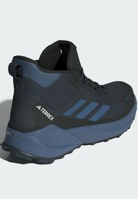 Bota de senderismo impermeable en negro y azul con parte superior texturizada, puntera reforzada y suela robusta. Presenta tres franjas azules y una lengüeta en el talón.