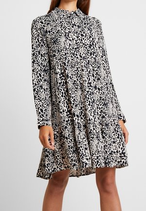 Sukienka w zwierzęcy wzór na beżowym tle z czarnymi plamkami. Długie rękawy, wysoki kołnierz oraz rozkloszowany, warstwowy dół.
