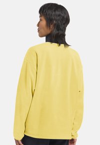 Maglione in pile giallo oversize con una finitura testurizzata. Presenta un collo alto e spalle cadute per un fit rilassato.