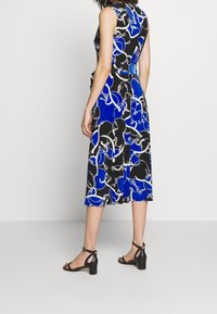 Sukienka midi bez rękawów w czerni i niebieskim z wzorem w łańcuch. Lekka tkanina, w kształcie litery A, zestawiona z czarnymi sandałami na słupku.