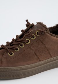 Sneaker en cuir marron avec doublure en fourrure, œillets en laiton, lacets ronds marron et semelle en caoutchouc texturé sur fond blanc.