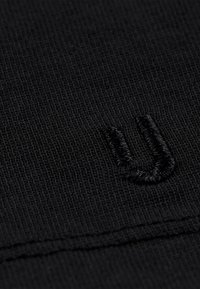 Czarna tkanina o wzorze dzianiny z teksturą oraz naszytym logo w kształcie litery "U". Zbliżenie pokazuje drobne detale i gładką powierzchnię.