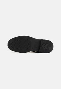 Suela de zapato de goma con surcos profundos, que presenta un patrón en zigzag y una zona lisa y plana cerca del talón para estabilidad y tracción.