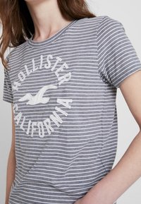 Grårandig t-shirt i bomull, med rund hals och framsidan med grafiskt tryck av en fågel med texten "Hollister California".