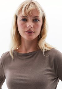 Lange mouwen, getailleerd top in zachte, bruine stof, met een ronde halslijn en een gladde textuur, gedragen met minimale accessoires.