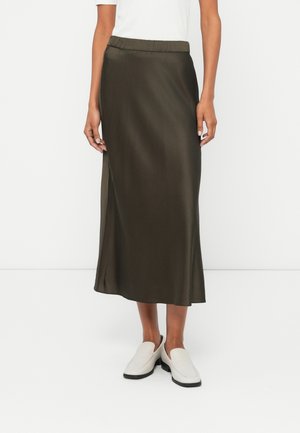 Jupe midi en satin vert olive avec une taille élastique et une fente sur le côté ; associée à des chaussures à enfiler de couleur claire.