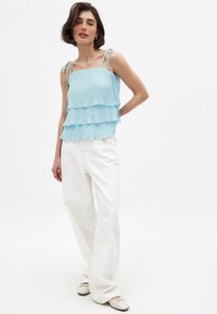 Hele sinine, volditud tank top kihilise disainiga ja reguleeritavate sidumislintidega, sobitatud valgete laia säärega pükstega ja lamejalatsitega.