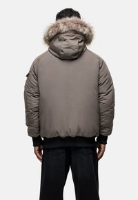 Giacca a imbottitura in un colore taupe tenue con cappuccio rimovibile foderato in pelliccia, polsini a costine e orlo arrotondato per una vestibilità aderente.