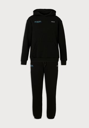 Sort sweatshirt og joggers sæt lavet af blødt stof. Har hætte, forlommer og blå tekstdetaljer på brystet og låret.