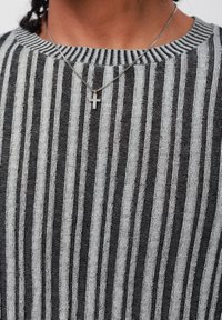 Persona che indossa un maglione a righe bianche e nere e una collana con croce argento su una catena argentata, mostrata dalla gola al petto.