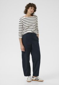Long-sleeve striped top in cream and navy, paired with navy wide-leg trousers and white sneakers with black stripes, featuring a relaxed fit.