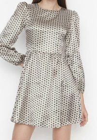 Femme portant une robe à manches longues, de longueur genou, avec un motif à carreaux noir et blanc et une taille cintrée.