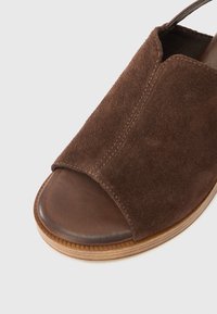 Καφέ σαμουρένια σαγιονάρα με ανοιχτή μύτη και λείο δερμάτινο πάτο. Διαθέτει ανάγλυφη ξύλινη σόλα για καλύτερη πρόσφυση και στήριξη.