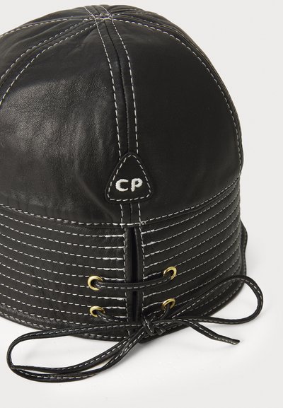 Chapeau en cuir noir avec des coutures blanches et des œillets en or, comportant une étiquette triangulaire avec le logo "CP" et un système de fermeture en lacet à la base.