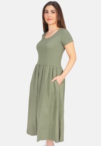 Olivengrünes Kleid mit kurzen Ärmeln, tailliertem Oberteil und gerafftem Rock. Verfügt über Seitentaschen und einen runden Ausschnitt. Leichter Stoff.