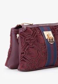 Borsa bordeaux con un frontale in velluto testurizzato a motivi floreali, un lato in pelle liscia e un accentuato hardware dorato con un dettaglio a righe.