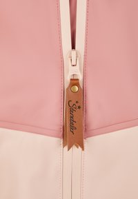 Eine pinke und cremefarbene Tasche mit Reißverschluss, die eine glatte Oberfläche, einen kontrastierenden Reißverschluss mit einem Lederetikett, das mit "Sterntaler" markiert ist, und eine ordentliche Naht hat.