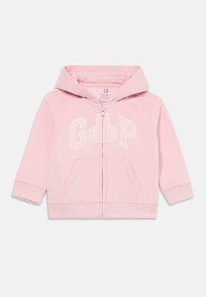 Felpa con zip di colore rosa chiaro, realizzata in tessuto morbido. Caratterizzata da un cappuccio, tasche frontali e logo "GAP" con un design di orsetto in bianco.