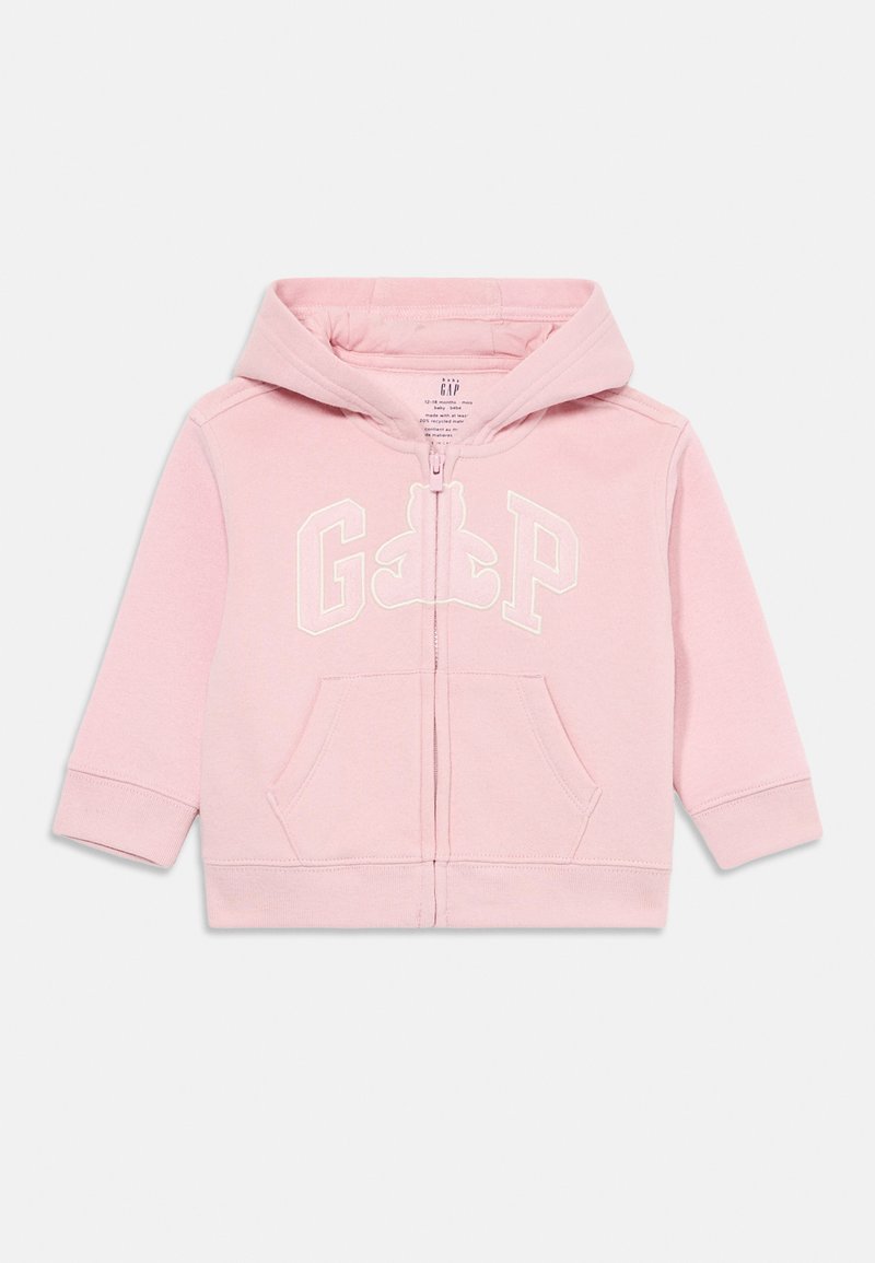 Felpa con zip di colore rosa chiaro, realizzata in tessuto morbido. Caratterizzata da un cappuccio, tasche frontali e logo "GAP" con un design di orsetto in bianco.
