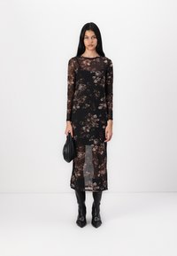 Robe noire transparente à manches longues, avec des motifs floraux marron et beige, mi-longue, avec une fente à l'avant. Assortie à des bottes noires à bout pointu et un sac noir.