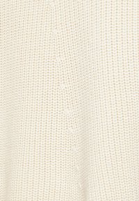 Stickad krämfärgad tröjfabric med en texturerad, ribbad design. Mjukt, lätt material med en subtil lyster och jämn söm.