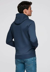 Sweat à capuche bleu marine en tissu mélange de coton. Caractéristiques : coupe décontractée, poche kangourou, poignets et ourlet côtelés. Vue de dos montrant la capuche.