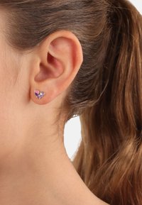 Orecchino a bottone in argento a forma di farfalla con accenti di smalto viola, forme delle ali distintive e una finitura lucida, indossato all'orecchio di un modello.