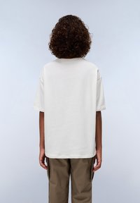 Cream cotton t-shirt with a relaxed fit, short sleeves, and a round neck. Worn with beige cargo pants, viewed from the back.