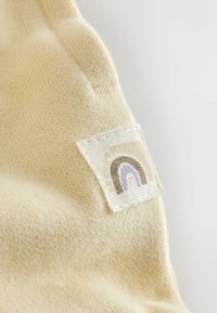 Heled kollane kangas pehme tekstuuriga, millel on tikitud plaastriga kujutatud vikerkaar pruunide, lilla ja kreemjat toonides.