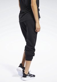 Pantalones de chándal negros con puños ajustados y un corte relajado, combinados con zapatillas deportivas en blanco y negro que tienen una suela texturizada y cordones.