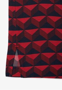 Tela de algodón con un patrón geométrico en rojo y azul marino, que presenta formas de cubo en 3D con acentos texturizados. Detalle de ventilación lateral con costuras rojas.